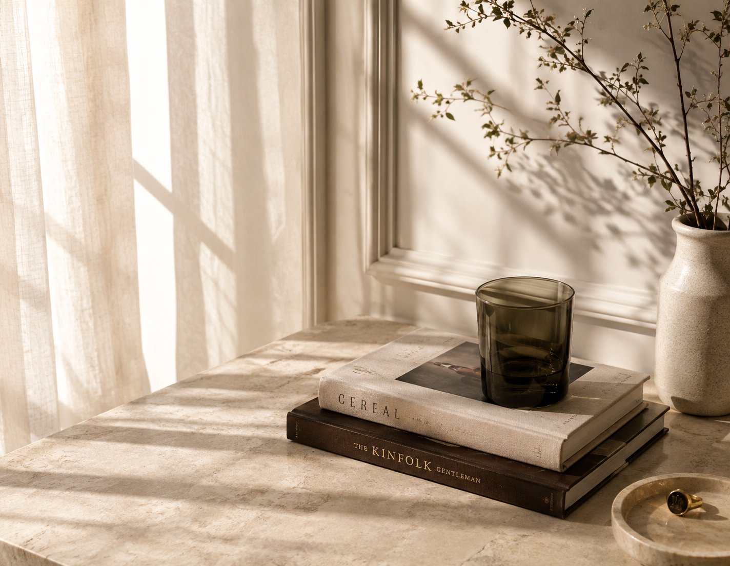 An &lsquo;old money&rsquo; still life &mdash; soft linen light on marble, a stack of design books, a green glass, a signet ring in a dish